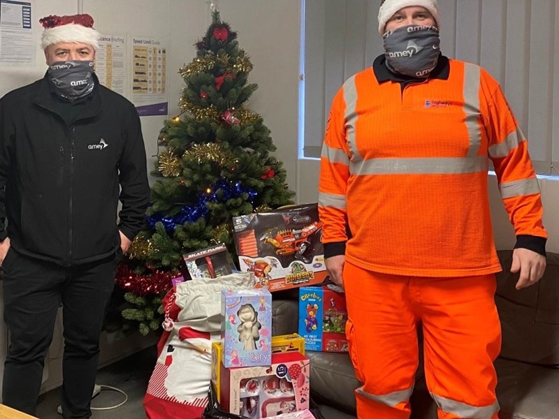 Amey employees wearing face coverings, during covid-19, stood in front of a Christmas tree and presents