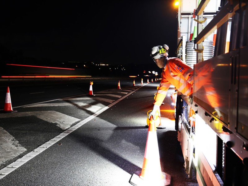 Image of a man placing traffic cones on the road at night.