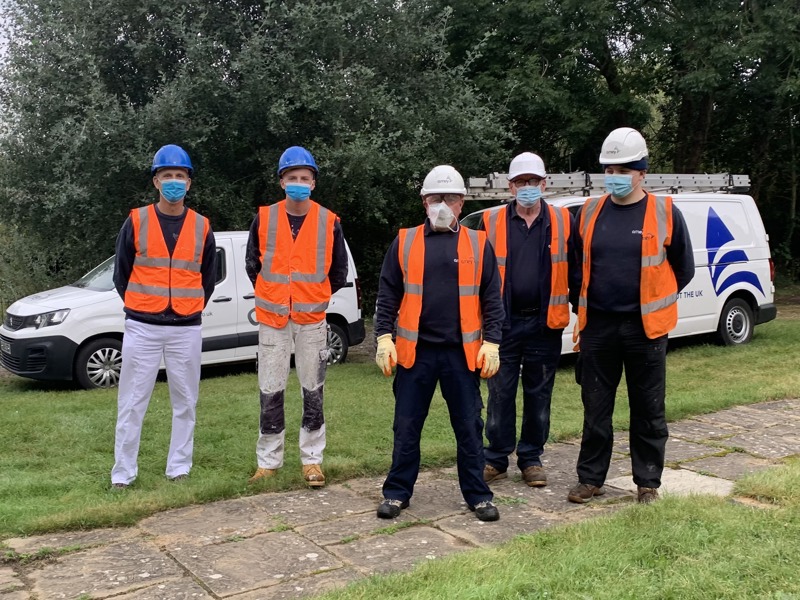 Image of five men stood in a row, wearing PPE and masks.