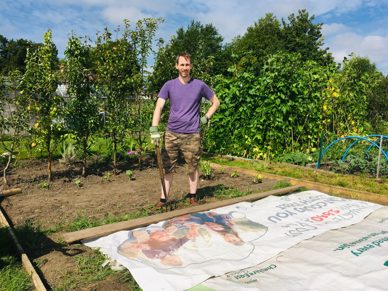 Image of an Amey employee in an allotment, holing a gardening fork in the ground.