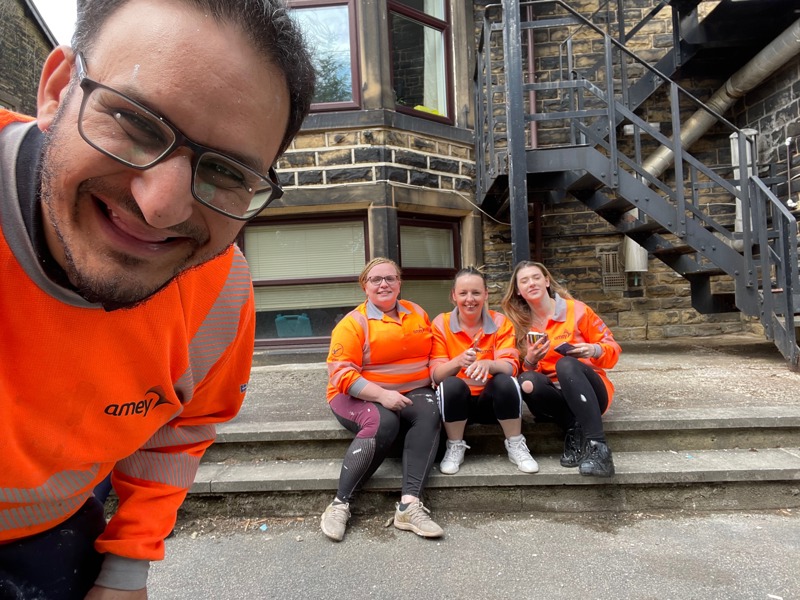 Image of three people sat on steps wearing Amey PPE, with a male at the forefront smiling.