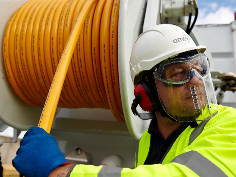 A man in PPE, pulling a hose from a reel.