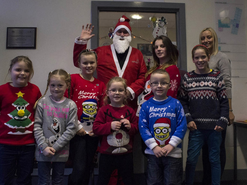 Man dressed as Santa, standing with children in Christmas jumpers.