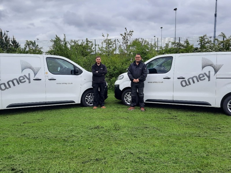 Image of two men stood in front of two new Amey electric vans.