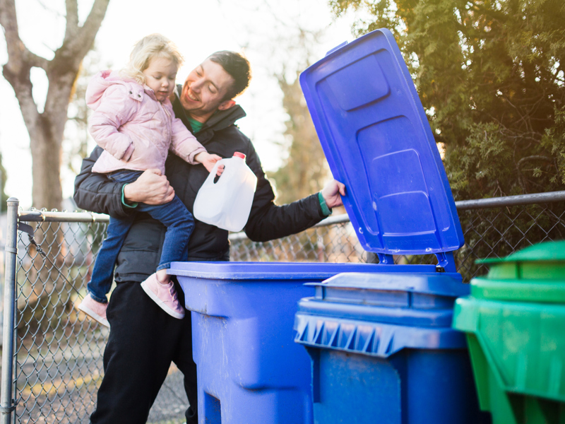 A man and child putting a milk carton in a bin.