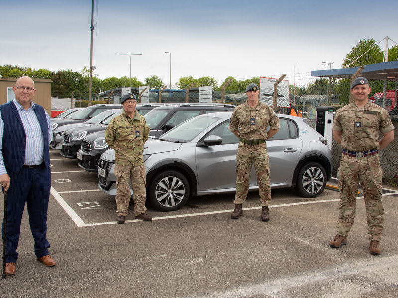 Military personnel standing in front of an EV charging parking area.