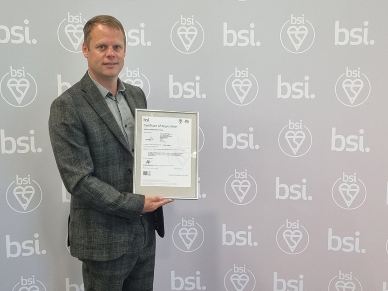 Image of an Amey employee, holding a certificate in front of a BSI backdrop.