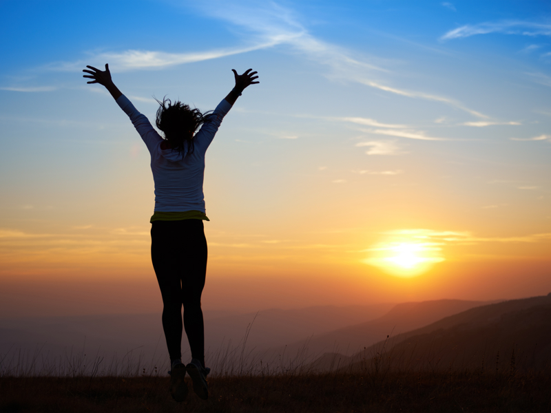 Image of a person raising their hands freely in front of a sunset.