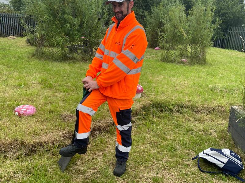 Image of a Amey employee, wearing PPE, stood on a spade in grass.