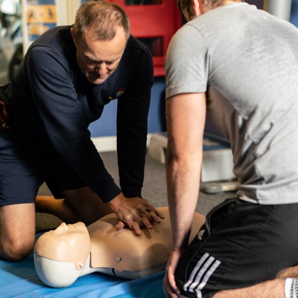 Two men undertaking CPR training on a dummy