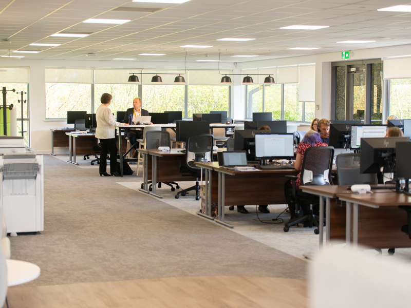 Image of an office with people sat at rows of desks.