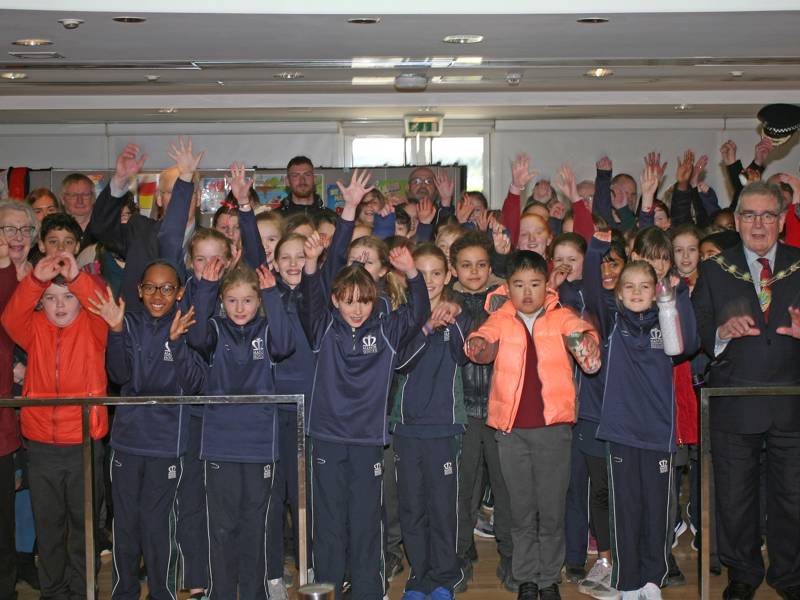 A image of a large group of school children holding their hands in the air.