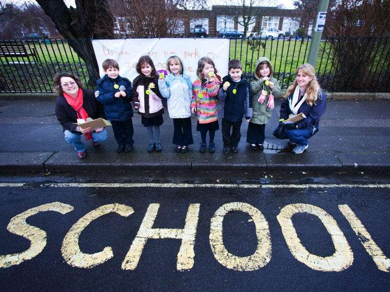 School children stood in front of a 'school' sign on the road.