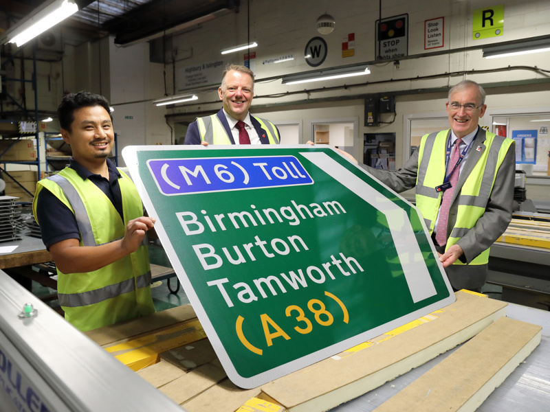 Image of people in PPE, holding a M6 Toll sign.