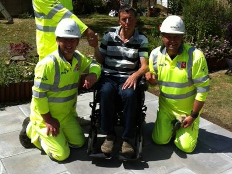 Three Amey employees, wearing PPE, stood with a man in a wheelchair.