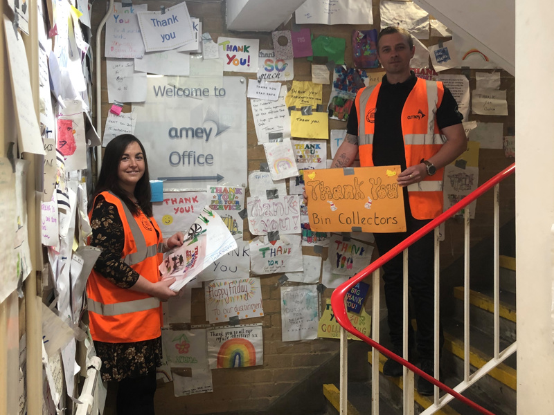 Two Amey employees stood in a corridor covered in letters of 'thank you' received from the community.