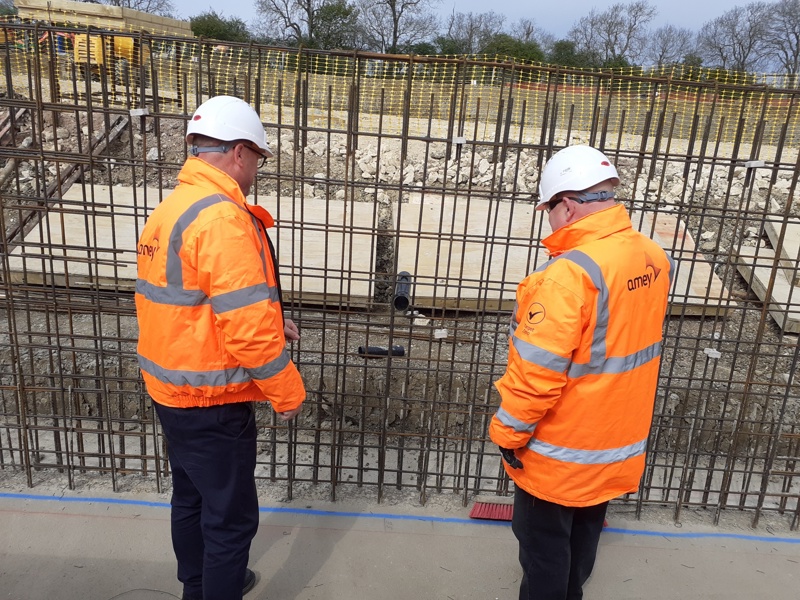 Image of two men in PPE with their back to us, stood in front of  a fenced off construction area.